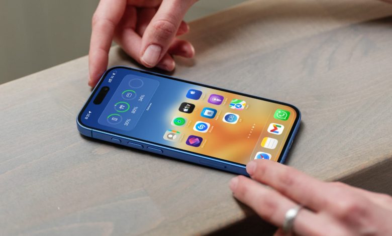 iPhone showing its beautiful Home Screen on a flat surface with a person’s hands on the top and bottom edges