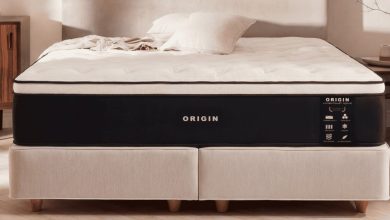 A professionally staged studio shot showcases the Origin LumbarCloud Hybrid mattress on a modern divan base in a bright, minimalist bedroom.