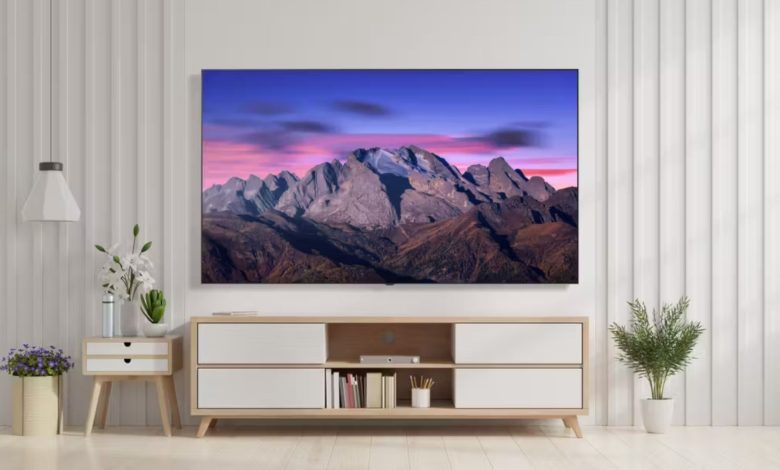 The LG B5 OLED displaying a mountain range at sunrise. The TV is wall-mounted in a bright, monochromatic living room setting above a credenza.