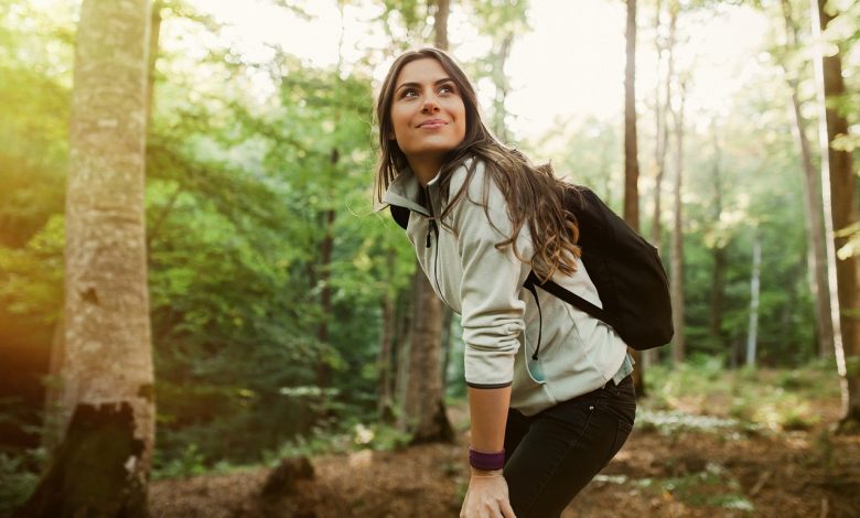 Woman in a forest wearing backpack and walking in nature smiling