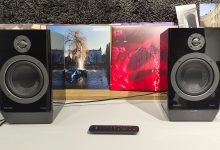 Philips Fidelio FA3 desktop speakers in front of busy bookshelf with remote control in between