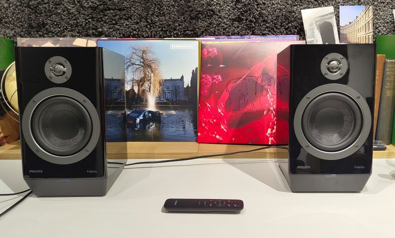 Philips Fidelio FA3 desktop speakers in front of busy bookshelf with remote control in between