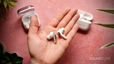 The Samsung Galaxy Buds 4 Pro and Apple AirPods Pro (3rd generation) earbuds resting in a hand over a pink textured surface with their charging cases in the background.