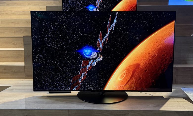 The Panasonic Z86C OLED TV pictured at a press event. On the screen is an image of a satellite orbiting an orange planet.