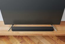 The Sony HT-SF150 soundbar positioned on a wooden cabinet, between the feet of a TV