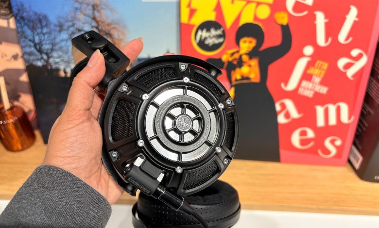 Yamaha YH-4000 open-back wired headphones held in hand in front of busy bookshelf