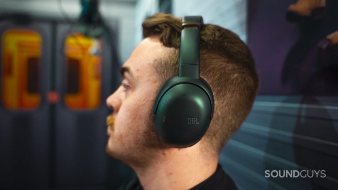 Person wearing green JBL over-ear headphones, side profile showing ear cup design and matte metallic finish.
