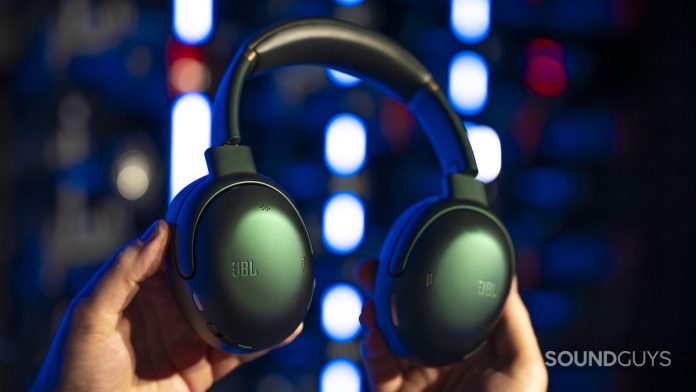 Hands holding green JBL over-ear headphones against a blurred background with colorful lights, highlighting both ear cups and headband.